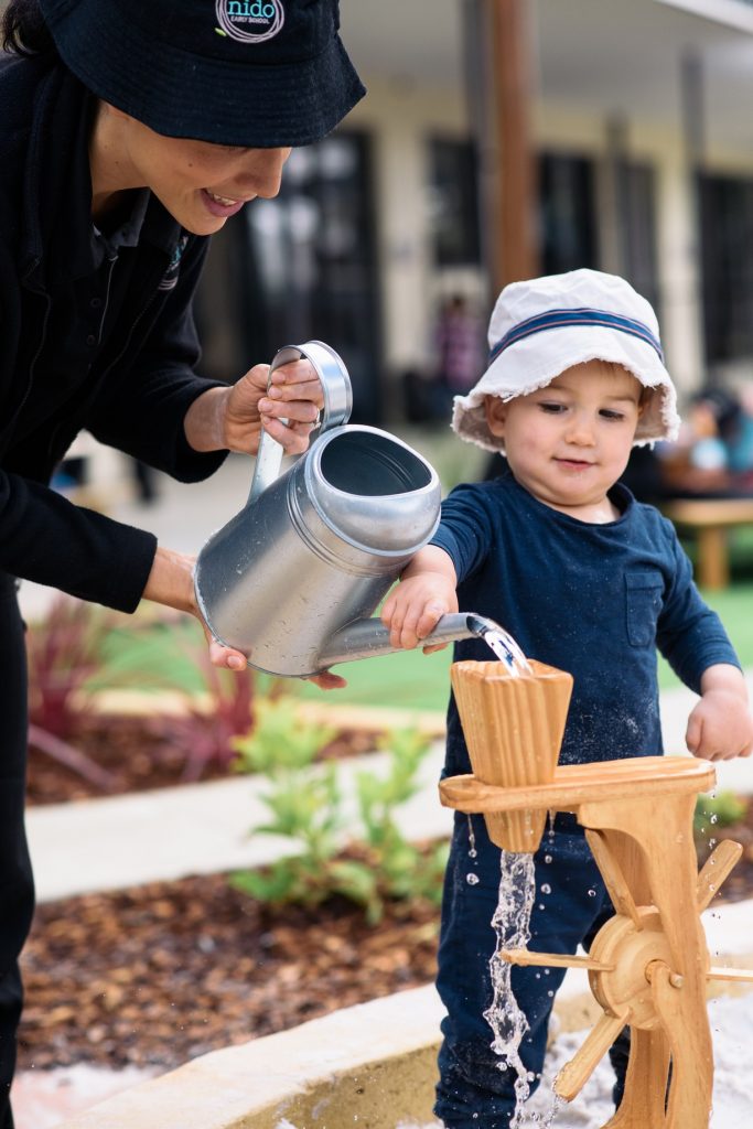Childcare educator helps a child with a water play activity